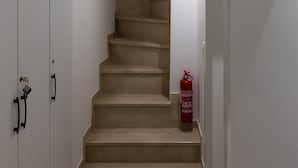 Un escalier aux marches de couleur beige menant à un palier, des murs blancs, un extincteur sur le palier et un paillasson noir au bas de l’escalier.