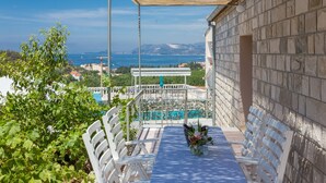 Una terrazza con tavolo e sedie, affacciata su una piscina e una vista panoramica del mare e delle montagne.