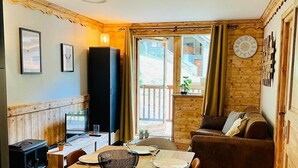 Un comedor acogedor con una mesa de madera preparada para cuatro personas, un sofá y un televisor al fondo.