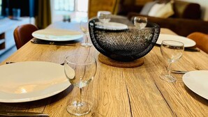 Una mesa de comedor dispuesta con platos, copas de vino, una cesta tejida y una mesa de madera.