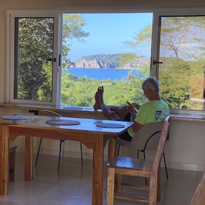 A person seated at a wooden table with a view of a coastal landscape through large windows.
