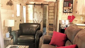 A cozy living room with a leather armchair and a brown sofa with red cushions. A small table with a remote control is visible. - Cozy Wooded Cabin in the Heart of RRG! (Campton)