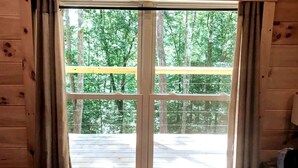 A wooden cabin with a large window offering a view of a deck and surrounding trees. - Cozy Wooded Cabin in the Heart of RRG! (Campton)