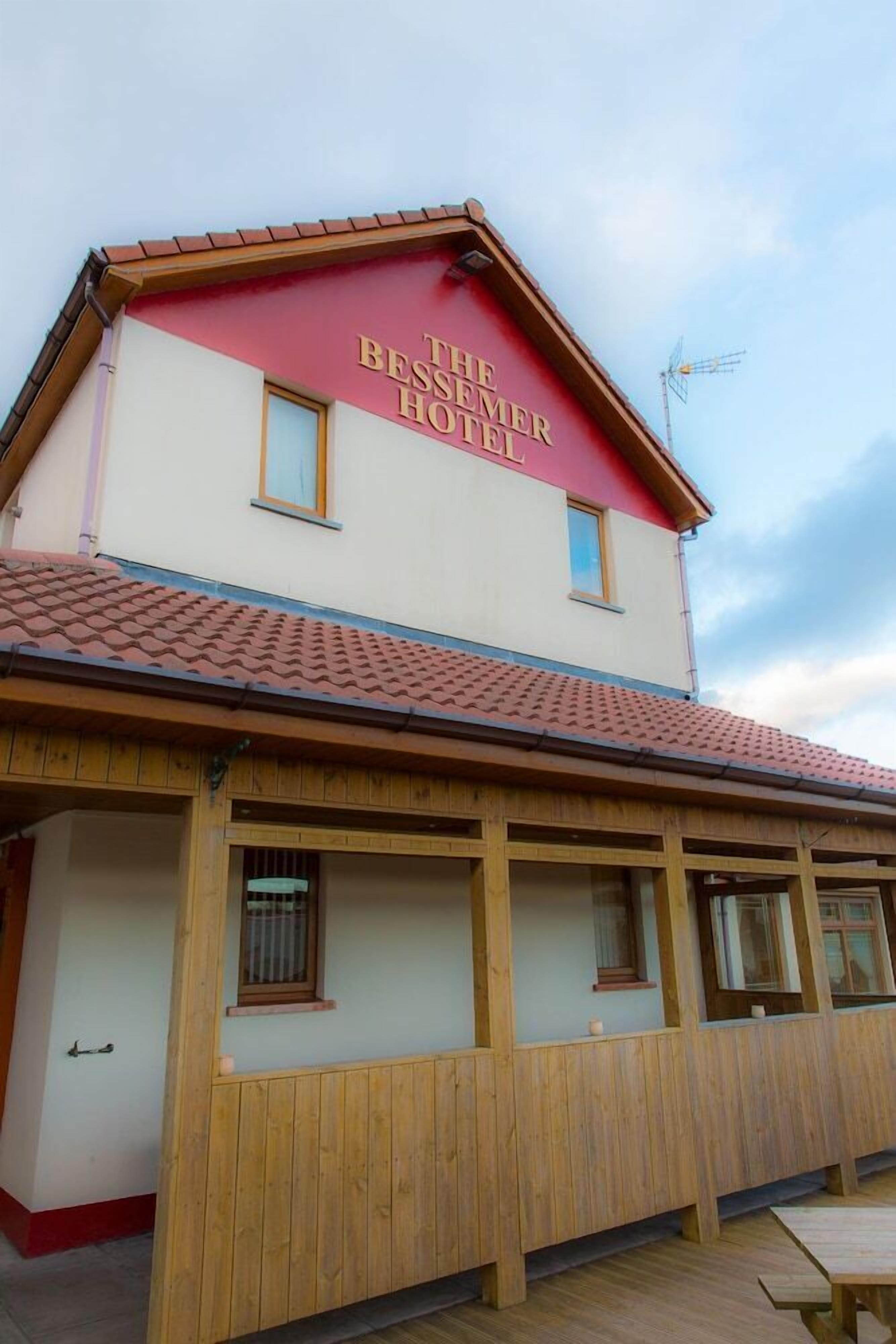 A two-story building with a red and white facade, labeled "The Bessmer Hotel." It features a tiled roof, wooden balcony railings, and multiple windows.