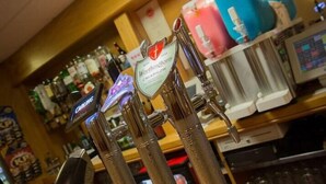 A bar area with multiple taps for different beverages, a clock, and shelves with various bottles in the background. - Bessemer Hotel (Merthyr Tydfil)