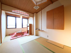 A traditional Japanese room with tatami flooring, a futon bed, a wooden wardrobe, and a sliding door. - Hotel Koryu (Fujikawaguchiko)