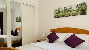 Un dormitorio con cama, mesita de noche, espejo y un cuadro de flores en la pared.