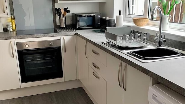 Una cocina moderna con armarios blancos, horno empotrado, lavavajillas y ventana con vistas.