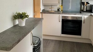 Una cocina compacta con armarios blancos, un horno de acero inoxidable, una pequeña planta en maceta y un reloj de pared.