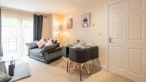 A modern living room with a grey sofa, black chairs, a glass coffee table, and a dining table set for four. - Apartment 5 (Worksop)