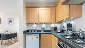 A compact kitchen with wooden cabinets, a built-in oven, a microwave, and a coffee maker. - Apartment 5 (Worksop)