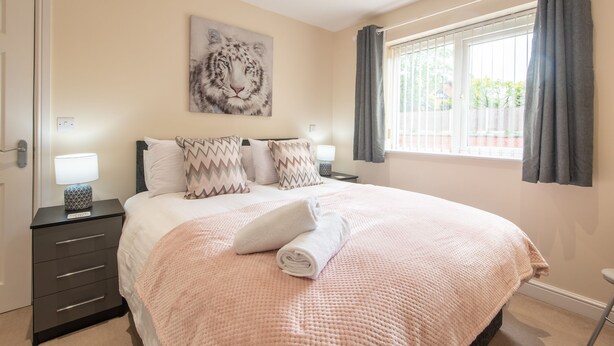 A bedroom with a large bed, a nightstand with a lamp, a painting of a tiger, and a window with curtains. - Apartment 5 (Worksop)