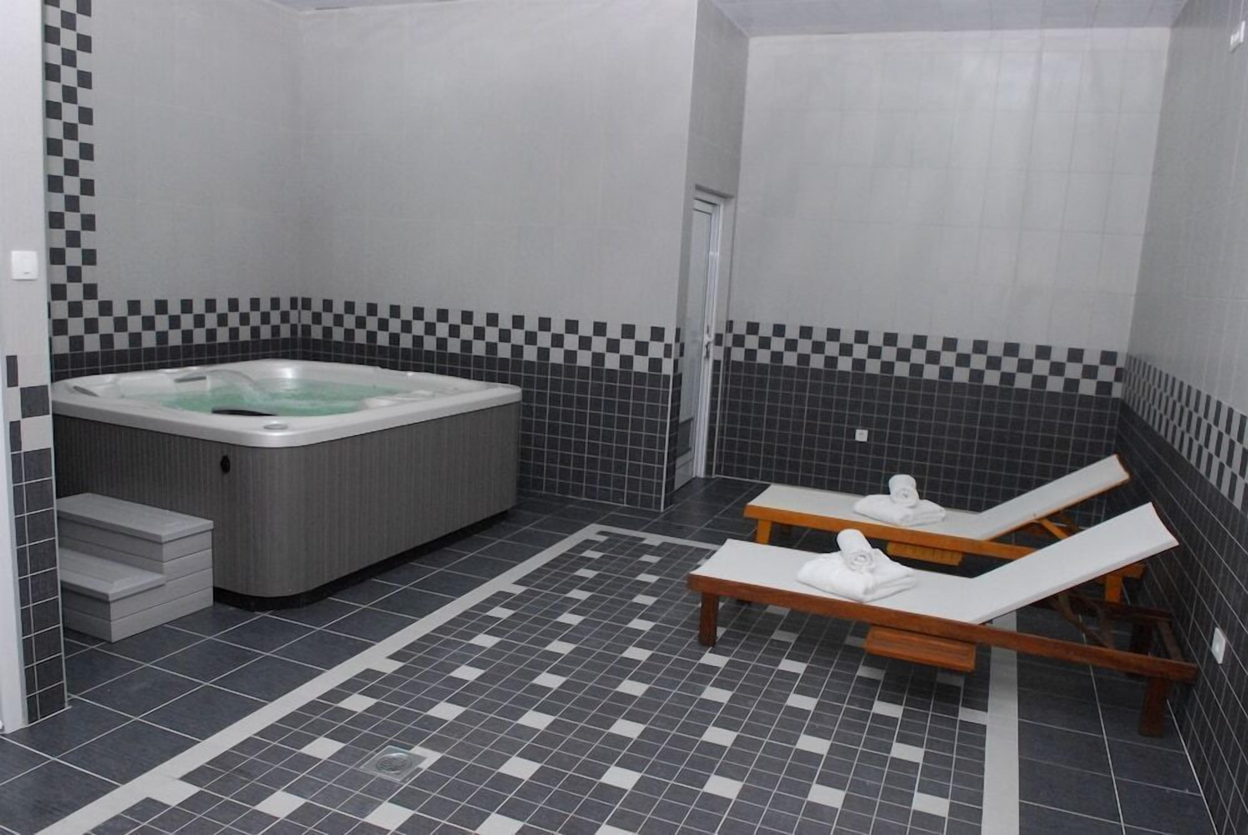Ein modernes Badezimmer mit einer großen Badewanne, zwei Liegestühlen und einem gefliesten Boden.