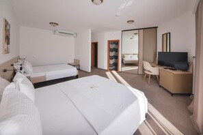 A hotel room with a large bed, a desk with a TV, a chair, and a small table. There is a mirror and a window with a view. - Hotel Magnolia (Tivat)