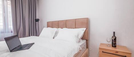 A bedroom with a bed, a laptop on the bed, a bedside table with a bottle and glass, and a lamp.