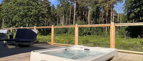 A hot tub on a wooden deck with a view of a forest.