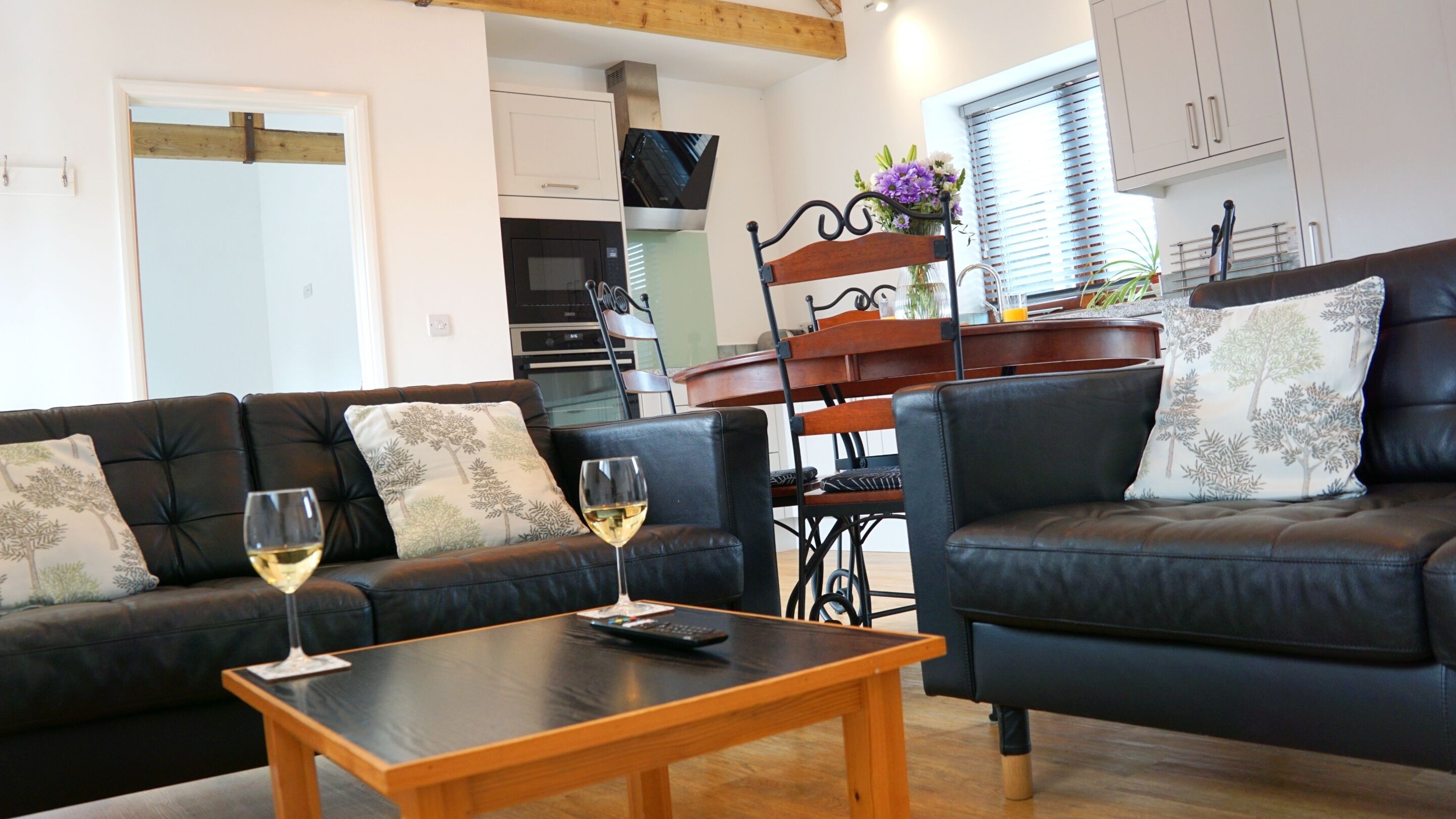 A living room with two black leather sofas, a wooden coffee table, and a dining area with a wooden table and chairs.