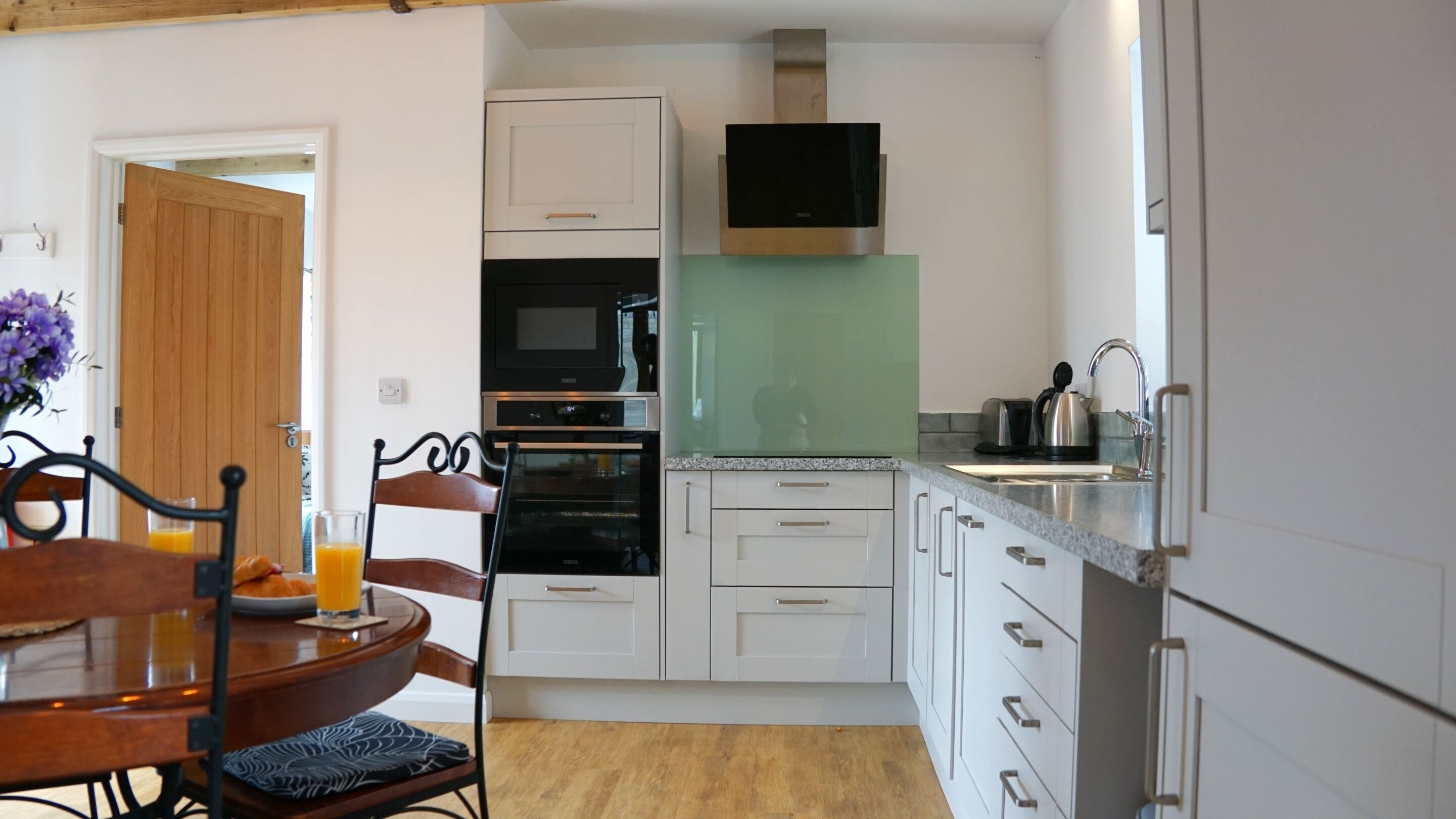 A compact kitchen with white cabinets, a microwave, oven, and a green backsplash.