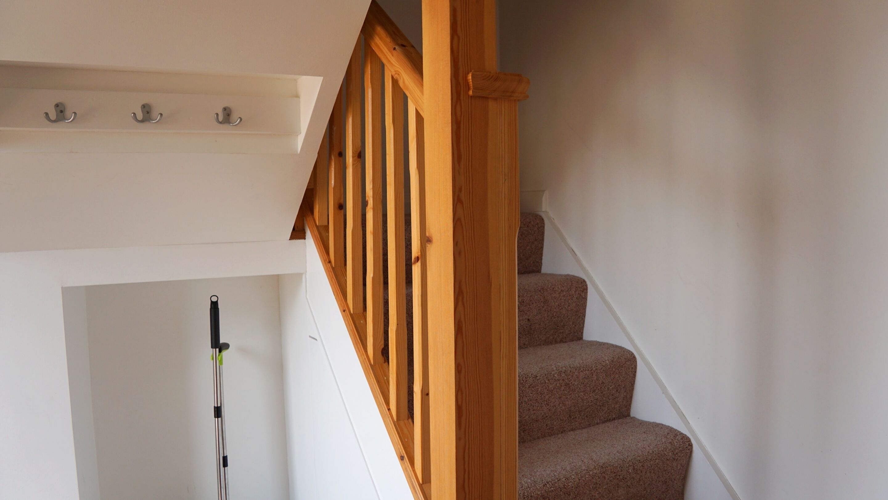 A wooden staircase with a handrail, carpeted steps, and a white wall.