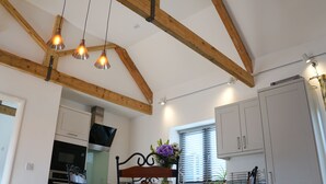 A kitchen with wooden beams, a dining table with chairs, a TV, and cabinets. - Courtbrook Farm Apartments (Exeter)