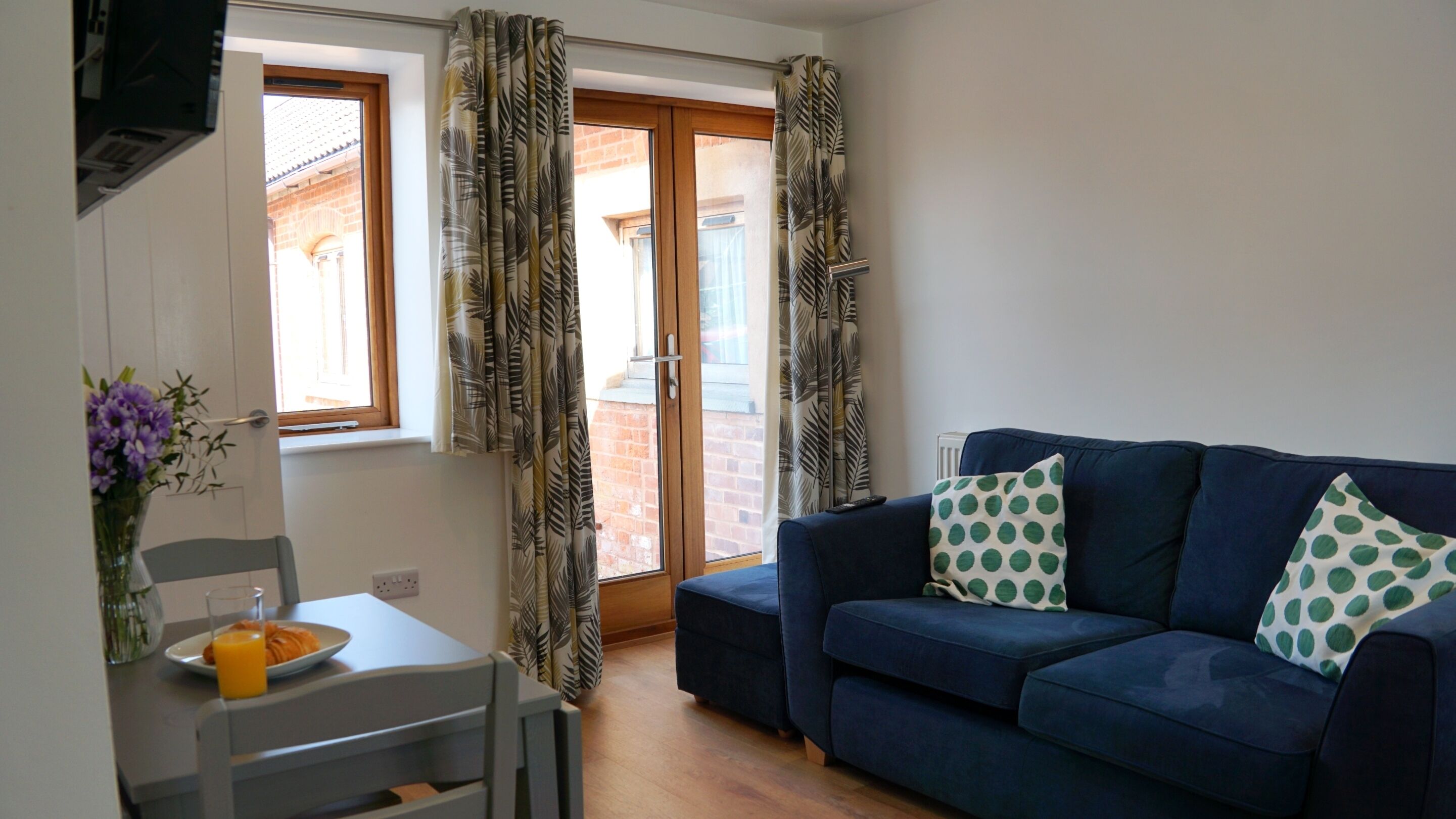 Una sala de estar con un sofá azul, una mesa de comedor con una silla y un ventanal con cortinas.