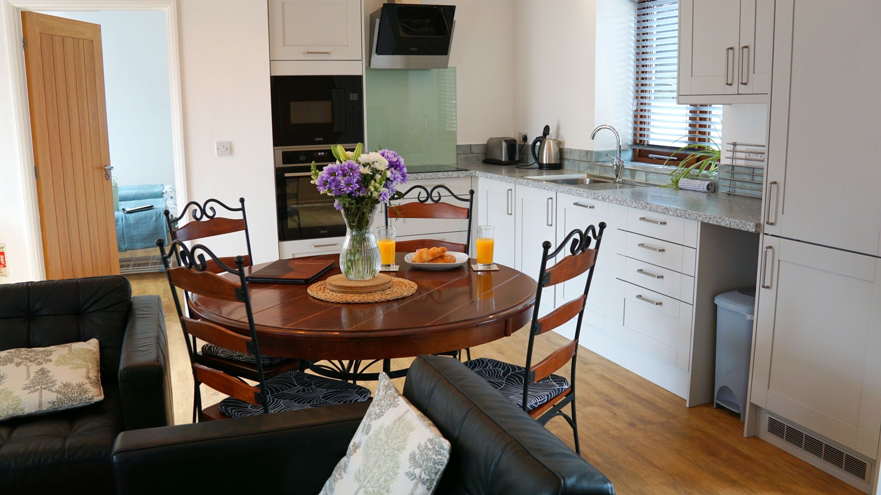 Een moderne keuken met witte kastjes, een eettafel met stoelen en een salontafel met een bloevas.