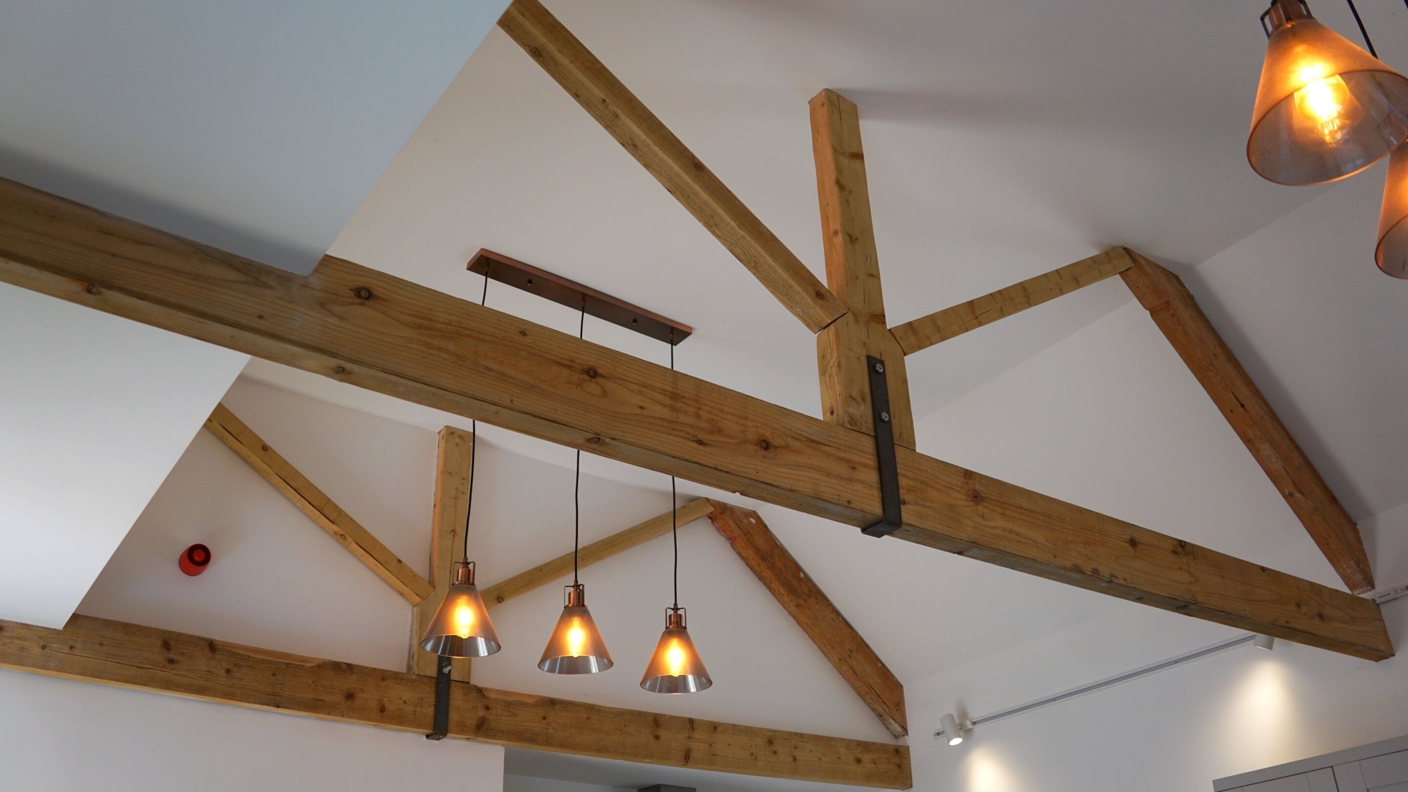 A room with exposed wooden beams, pendant lights, and a visible ceiling fan.