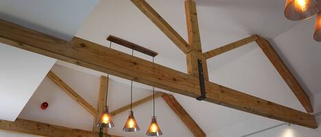 A room with exposed wooden beams, pendant lights, and a visible ceiling fan.