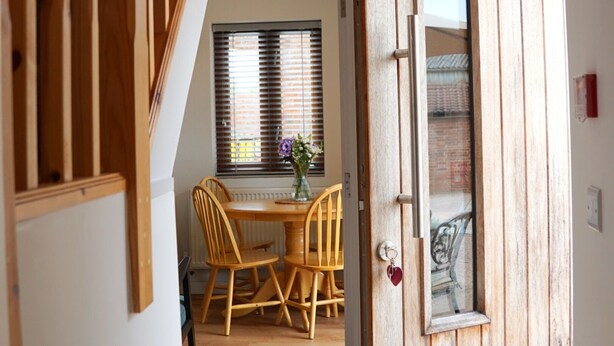 A wooden staircase leading to a dining area with a table and chairs, a window with blinds, and a door with a glass panel. - Courtbrook Farm Apartments (Exeter)