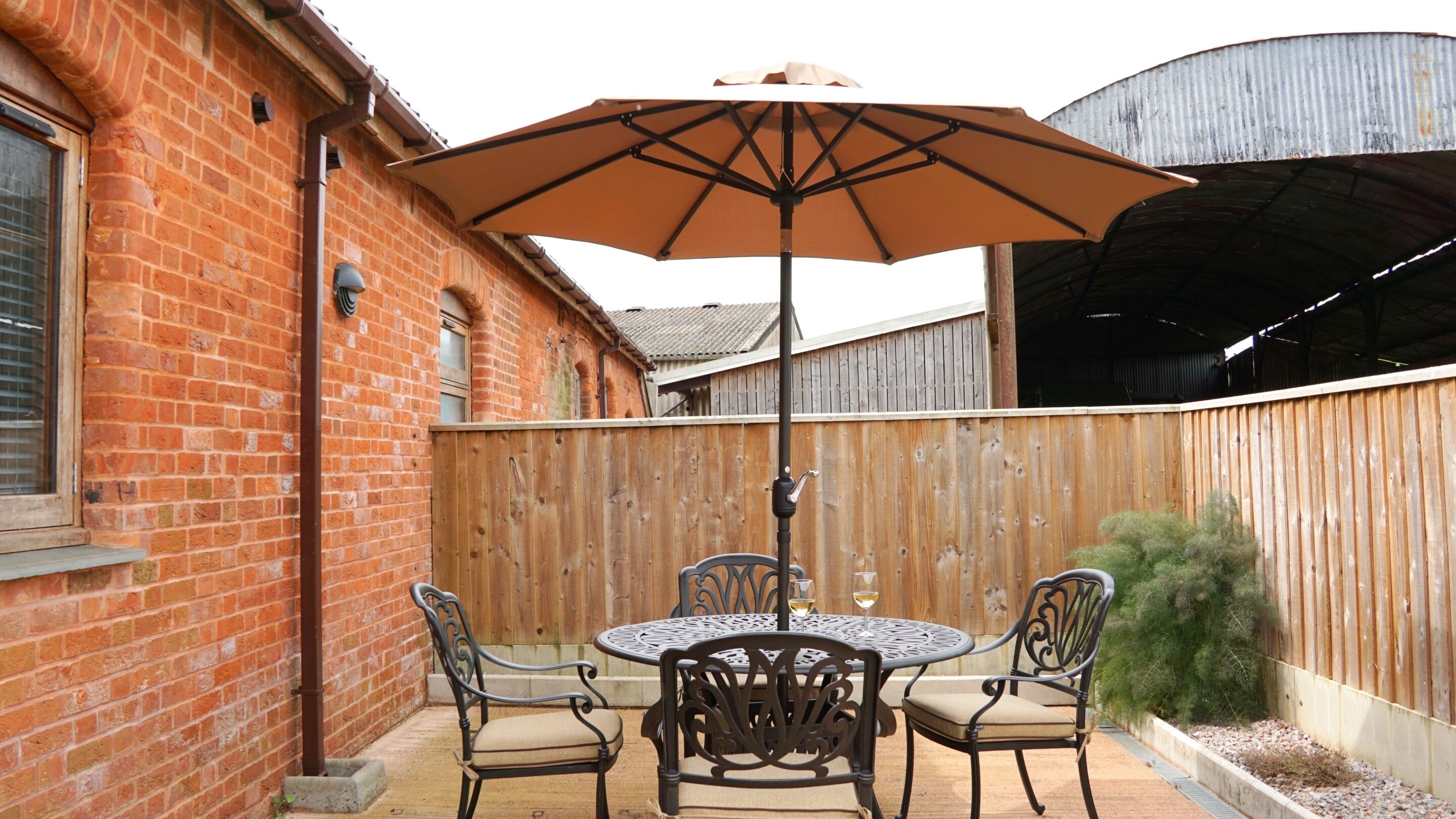 A patio with a round table and four chairs, an umbrella, and a wooden fence.
