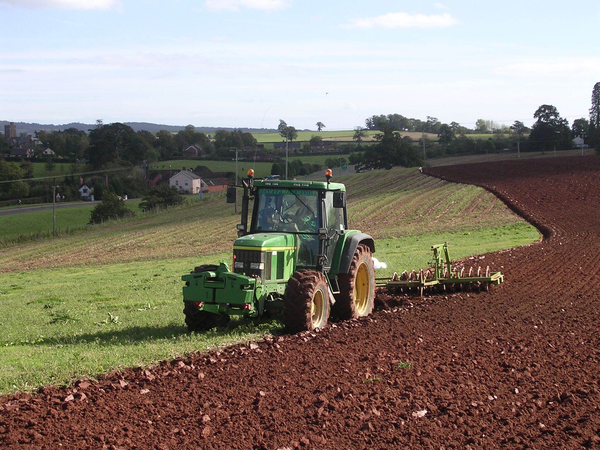 A green tractor with a plow attachment in a field.