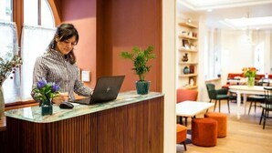A reception desk with a laptop, a potted plant, and a checkered uniformed staff member. - Bonsoir Madame (Paris)