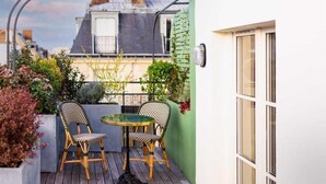 Un balcon avec deux fauteuils en osier et une petite table, entouré de plantes en pot et offrant une vue sur les bâtiments.
