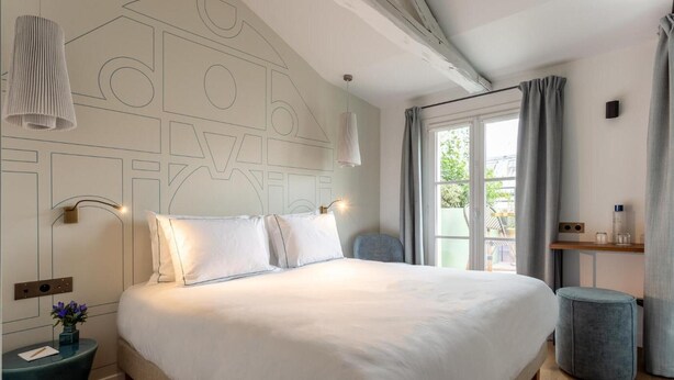 Une chambre d’hôtel moderne, dotée d’un grand lit, d’une table de chevet, d’une chaise et offrant une vue sur l’extérieur.