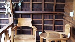 A wooden interior with a high ceiling, two wooden chairs, a small round table, and a wooden railing. - Puri Rasa Villas and Resort (Ubud)