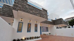 Un edificio moderno con fachada de piedra, ventanas con marco azul y una zona de patio con baldosas.