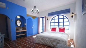 Un dormitorio con una cama grande, un baño con puerta azul y un ventanal con marco azul.