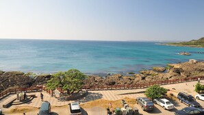 A coastal area with a paved walkway, parked cars, and a view of the sea.