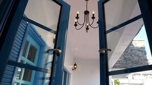 Vista a través de una ventana azulada, con candelabro, que muestra una fachada de piedra y una pared interior blanca.