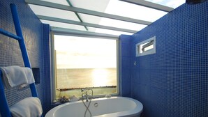 A bathroom with a bathtub, a window with a view of the sea, and blue tiled walls.