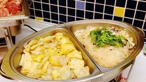 A buffet with various dishes including pasta, noodles, and a salad with greens.