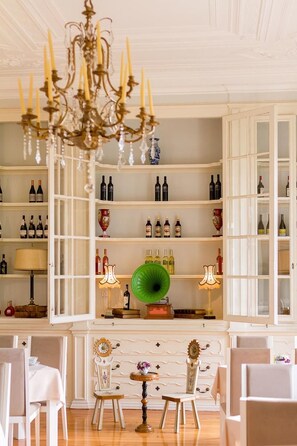 A room with a chandelier, shelves with bottles, a green decorative plate, and a table with chairs. - Palácio das Especiarias (Lisbon)