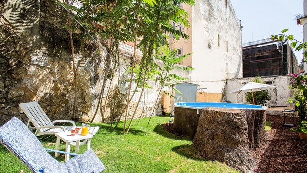 Un patio trasero con piscina, zona de barbacoa techada y mesa con sillas.