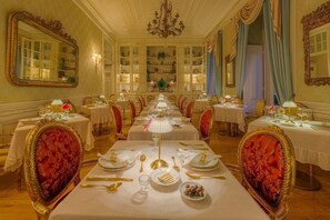 Un comedor formal con varias mesas dispuestas para el servicio, sillas ornamentadas y un candelabro.