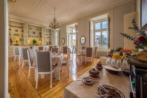 A dining area with white chairs and tables, a chandelier, and a view of the outside through large windows. - Palácio das Especiarias (Lisbon)