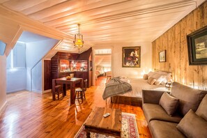 Una sala acogedora con techo de madera, un comedor con mesa y sillas, un sofá y una cama con colcha estampada.