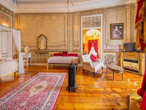 Una habitación con cama, una silla, una mesa, chimenea y espejo.