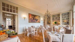 Un comedor con varias mesas y sillas, una araña de techo y una pared con un cuadro enmarcado.