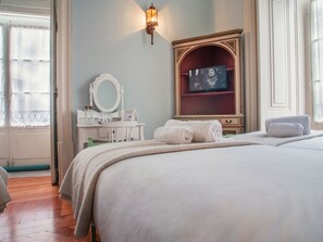 A hotel room with a large bed, a vanity with a mirror, a television, and a wall-mounted light fixture. - Palácio das Especiarias (Lisbon)