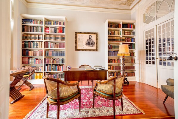 A library with bookshelves, a desk, chairs, and a framed picture on the wall. - Palácio das Especiarias (Lisbon)